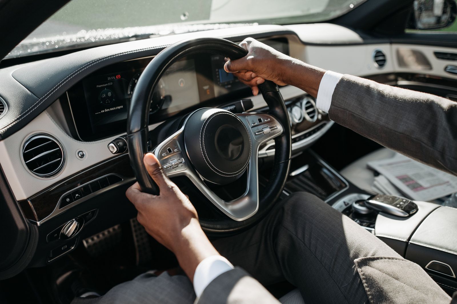 A chauffeur in a dark suit holds the rear door of a black sedan