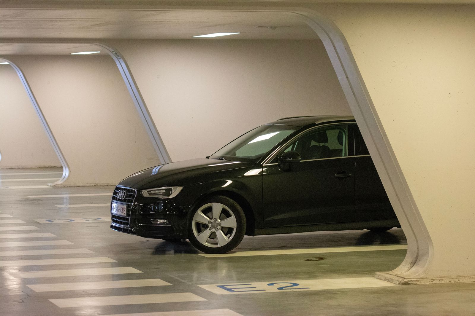 A black sedan waits in a loading bay beneath an office tower