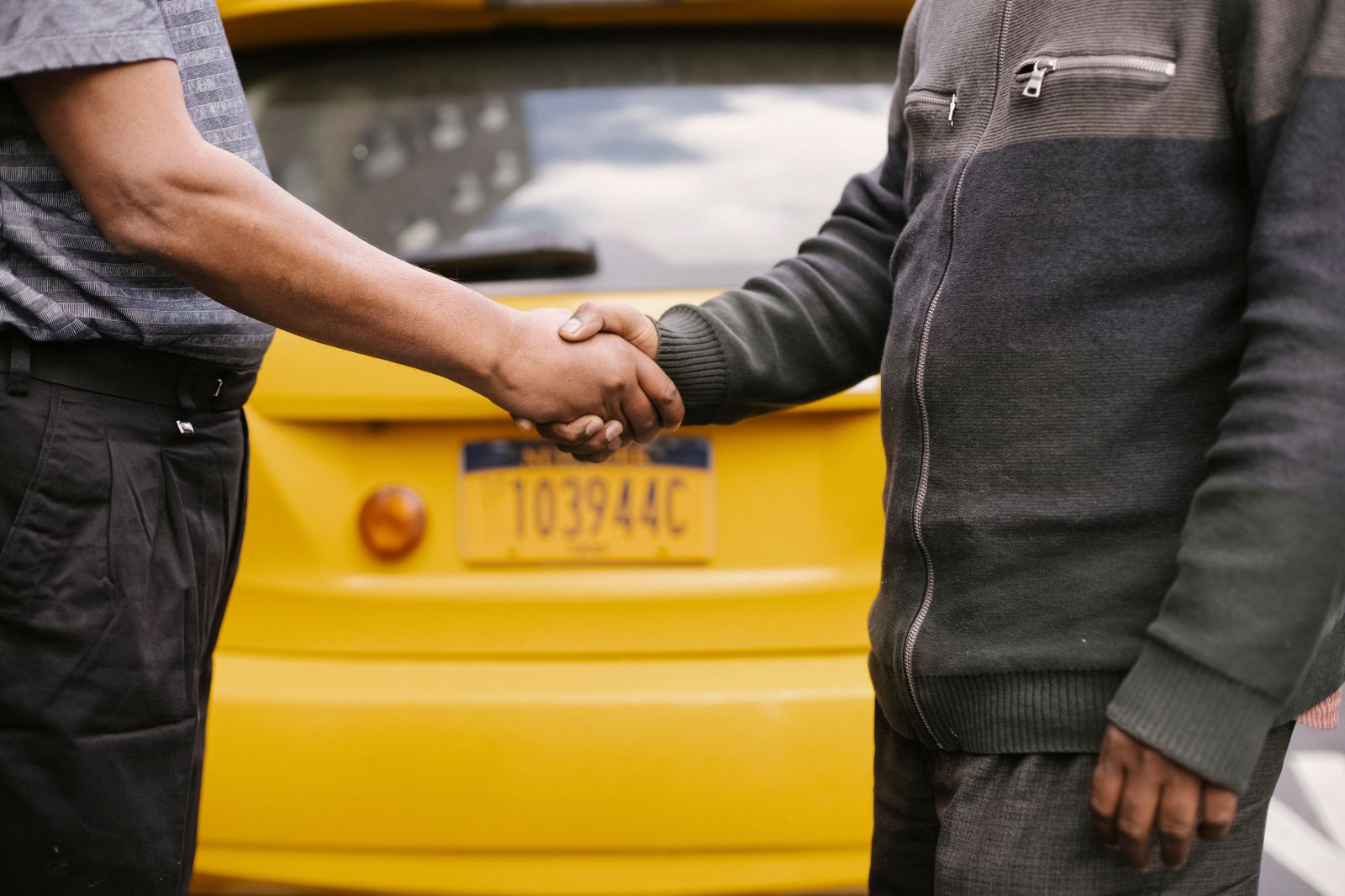 A chauffeur shakes a passenger's hand beside a black car